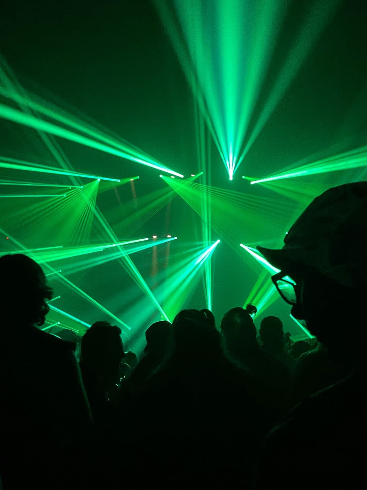 Green lasers cutting through haze above a rave crowd